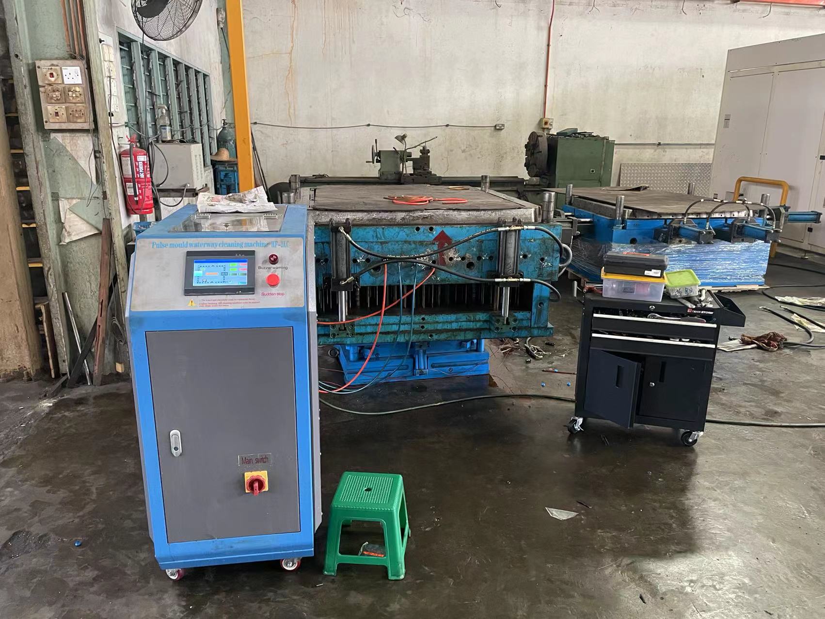 Injection mold tooling clamped in a machine on the factory floor, with mold-cleaning equipment nearby.